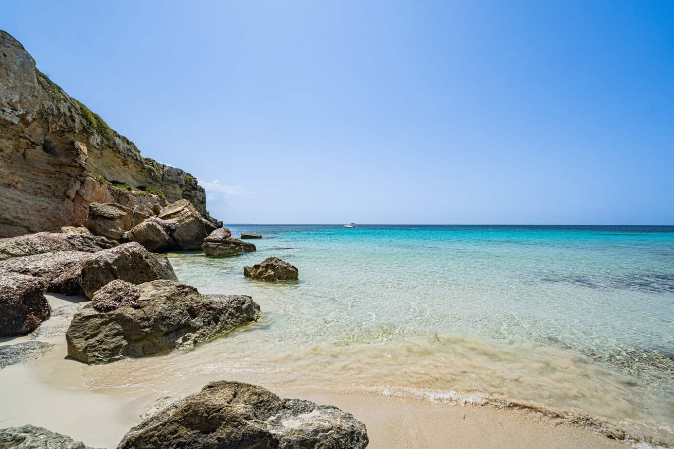Klares türkisfarbenes Wasser und sanfte Wellen treffen auf Favignana auf einen Sandstrand mit großen Felsen und einer Felsklippe.