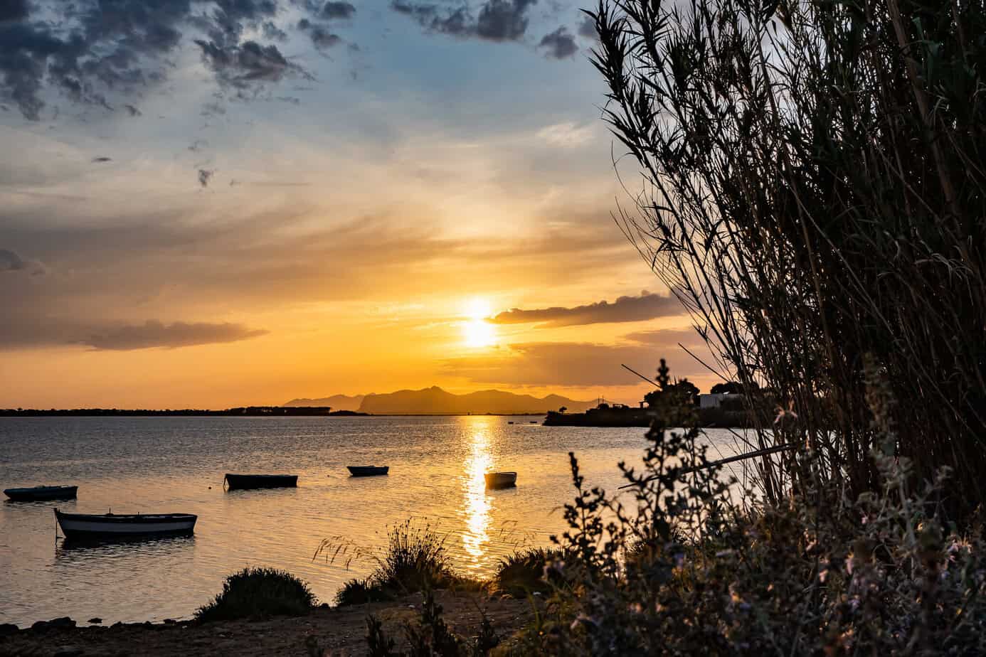 Ein goldener Sonnenuntergang über den Salinen von Marsala mit mehreren kleinen Booten, die auf dem Wasser treiben.