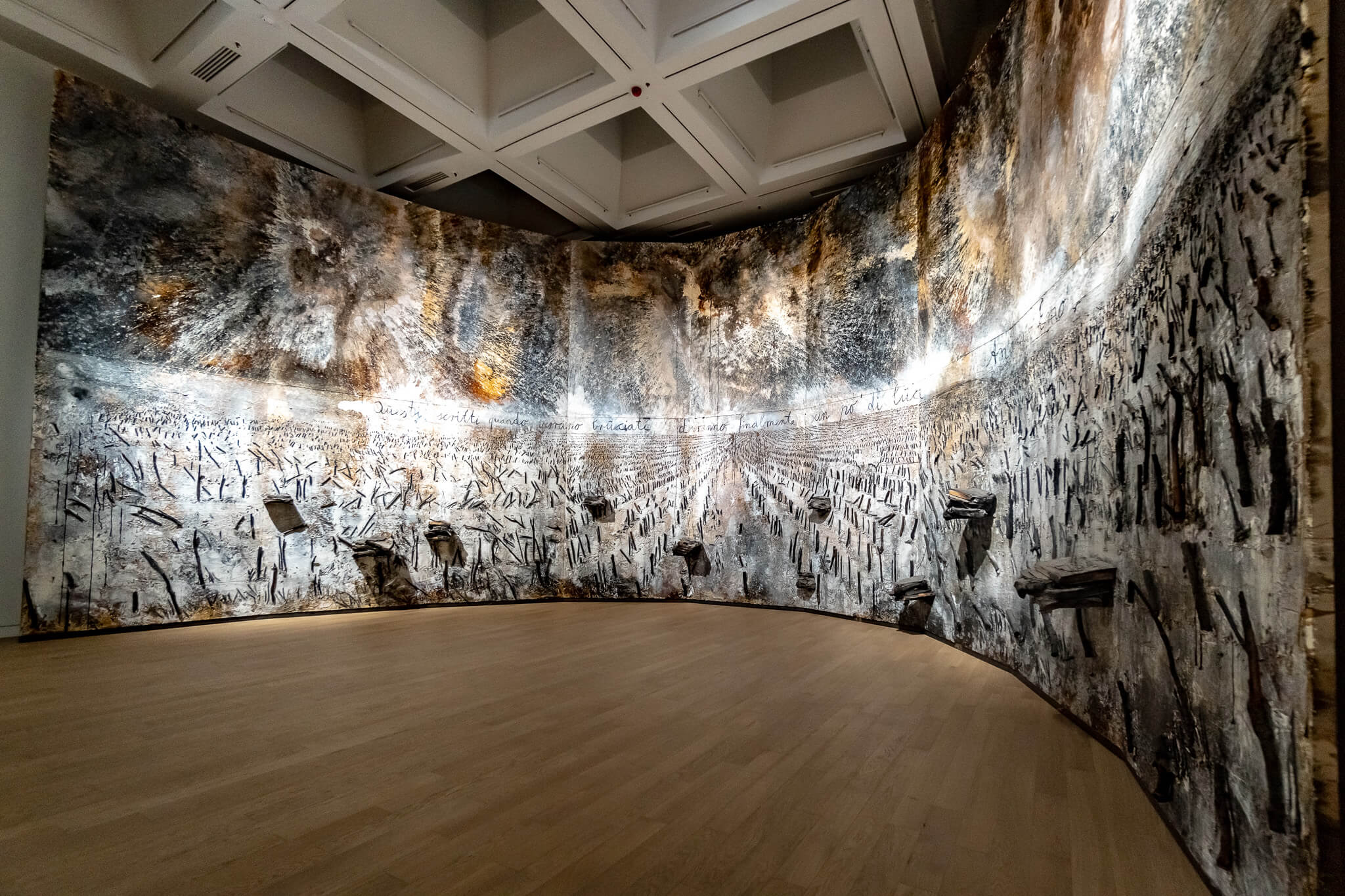 Almaty Sehenswürdigkeiten: Die schönsten Highlights & meine 8 Tipps 3 Gebogene, raumhohe Wand mit einem großformatigen grau-schwarzen Kunstwerk mit aufgesetzten Objekten in einem Ausstellungsraum mit Holzboden