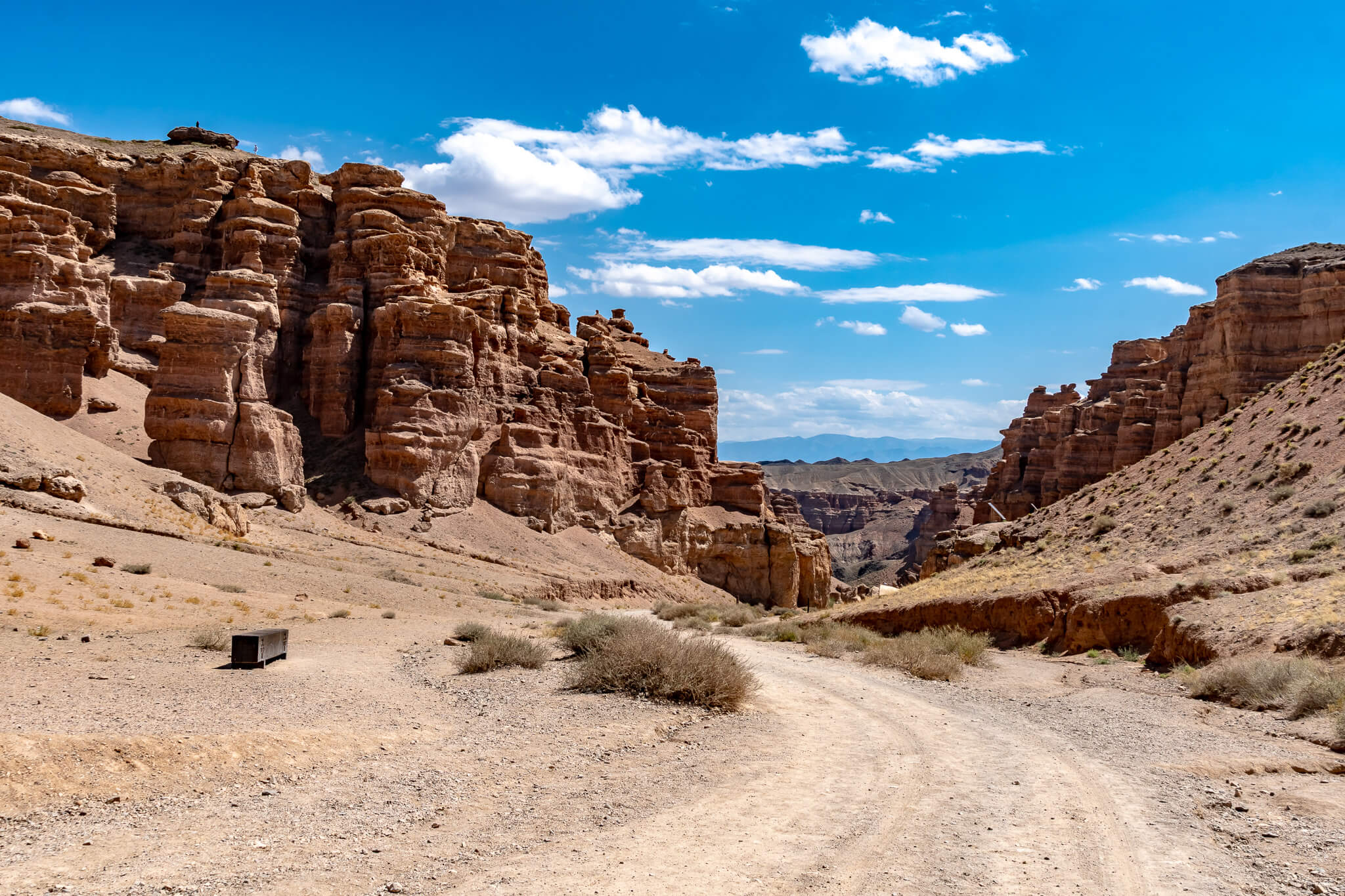 Almaty Sehenswürdigkeiten: Die schönsten Highlights & meine 8 Tipps 15 Rötliche, turmartig erodierte Felsformationen zu beiden Seiten eines Schotterwegs im Charyn Canyon unter blauem Himmel