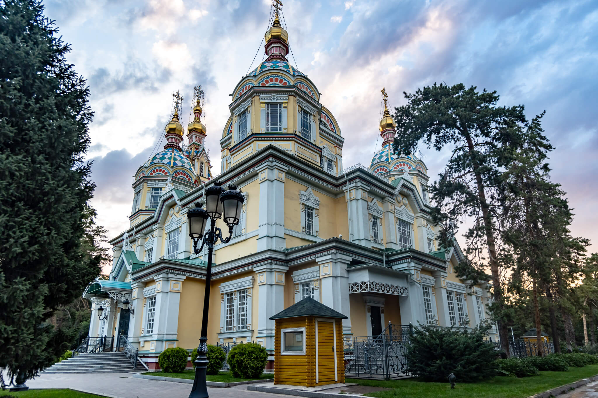 Almaty Sehenswürdigkeiten: Die schönsten Highlights & meine 8 Tipps 5 Gelb-weiße Fassade der Christi-Himmelfahrt-Kathedrale in Almaty mit bunten Kuppeln, umgeben von hohen Nadelbäumen